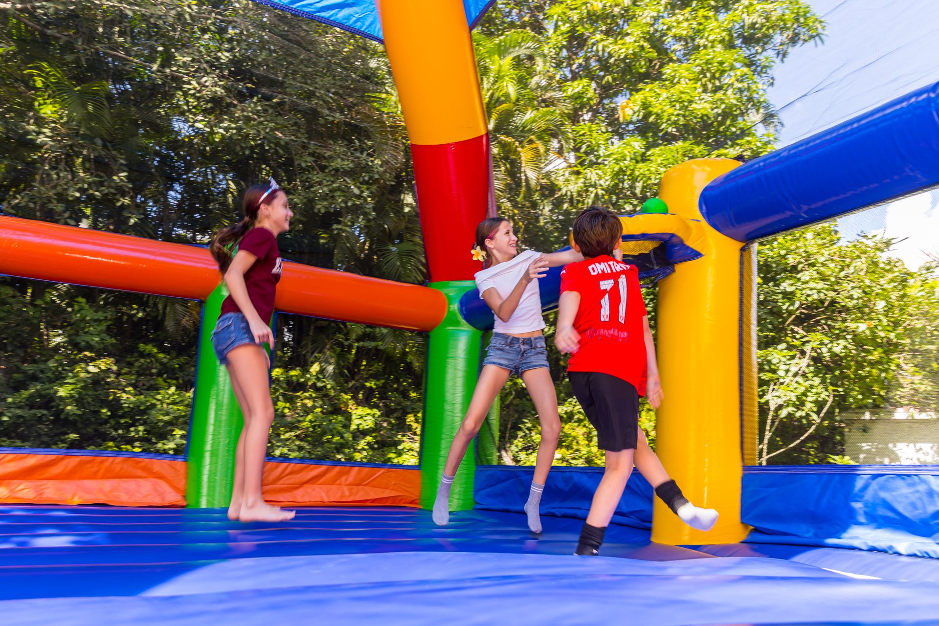 Two girls and a boy jump high inside the bounce house