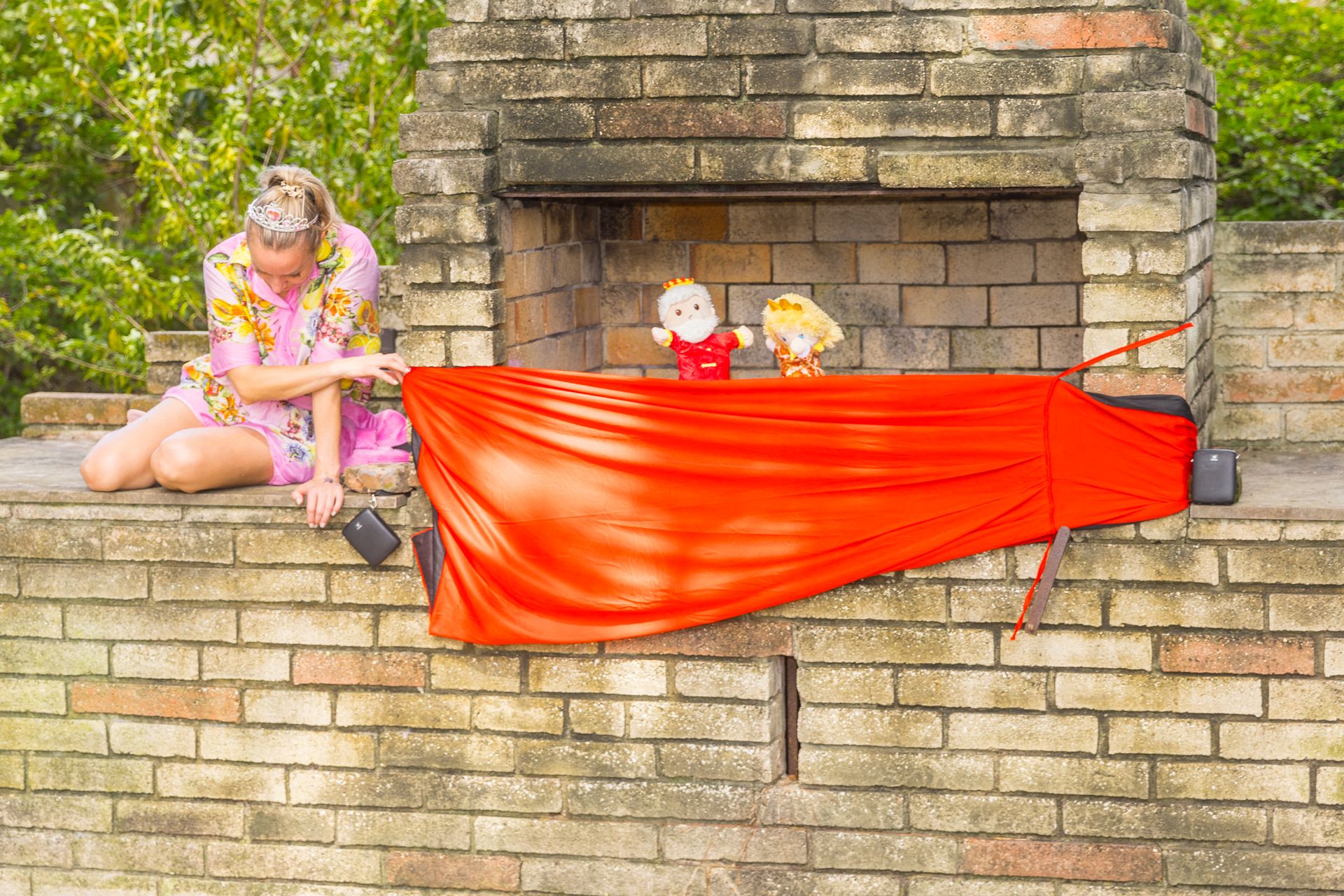 Katya behind a red curtain with the King and Queen puppets on a brick puppet stage