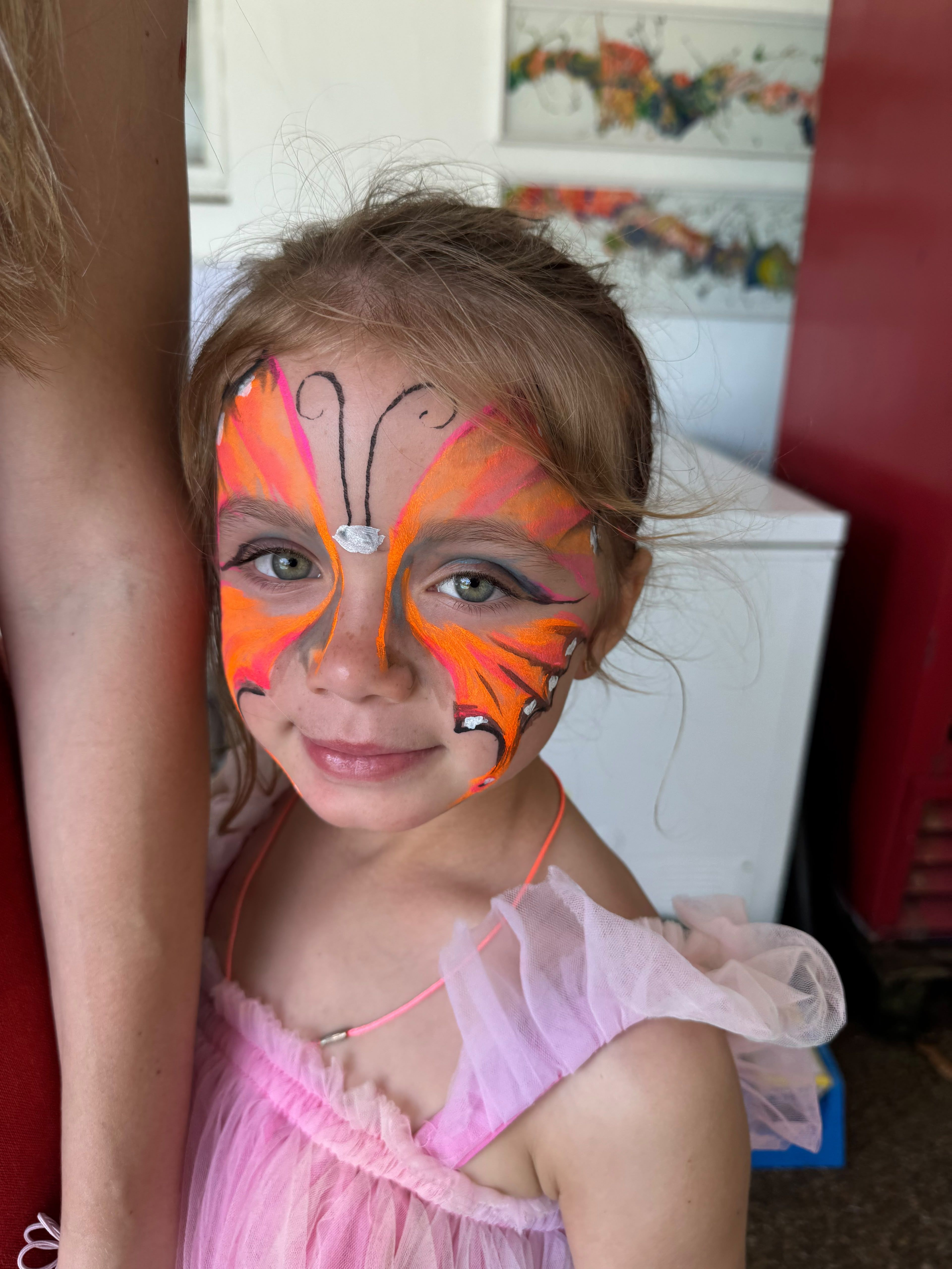 A smiling girl with an orange butterfly painted on her face